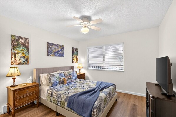 A bedroom with a bed, two bedside tables with lamps, a ceiling fan, and a TV stand.