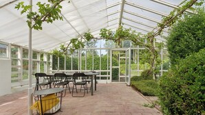 Ein Gewächshaus mit Tisch und Stühlen, umgeben von viel Grün.
