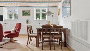 Ein Essbereich mit einem Holztisch und Stühlen, einem roten Sessel und einer Decke mit freiliegenden Balken.