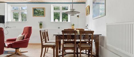 A dining area with a wooden table and chairs, a red armchair, and a ceiling with exposed beams.