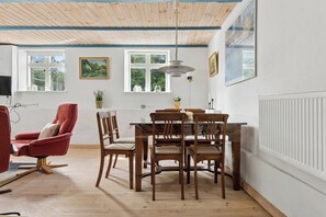 A dining area with a wooden table and chairs, a red armchair, and a ceiling with exposed beams. - Charming 45 m² house in peaceful setting (Gelsted)
