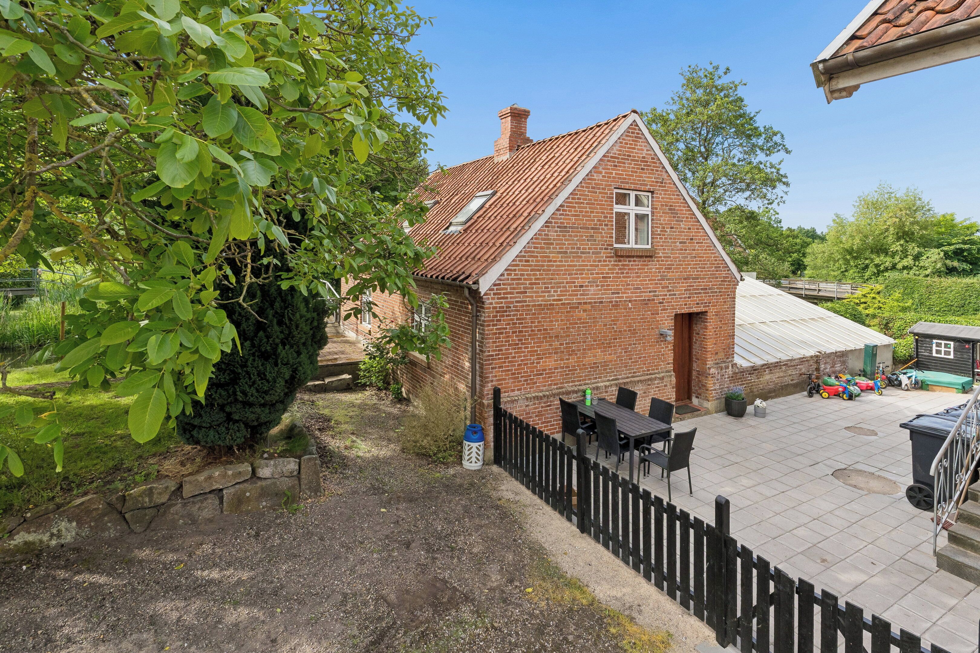 A brick house with a tiled patio, a fenced garden, and a small shed.