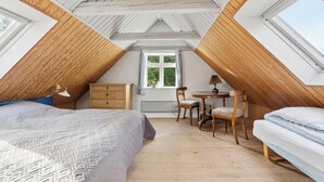 Ein Schlafzimmer mit schrägen Wänden, Holzbalken, einem Bett, einem Schreibtisch und einem Stuhl.