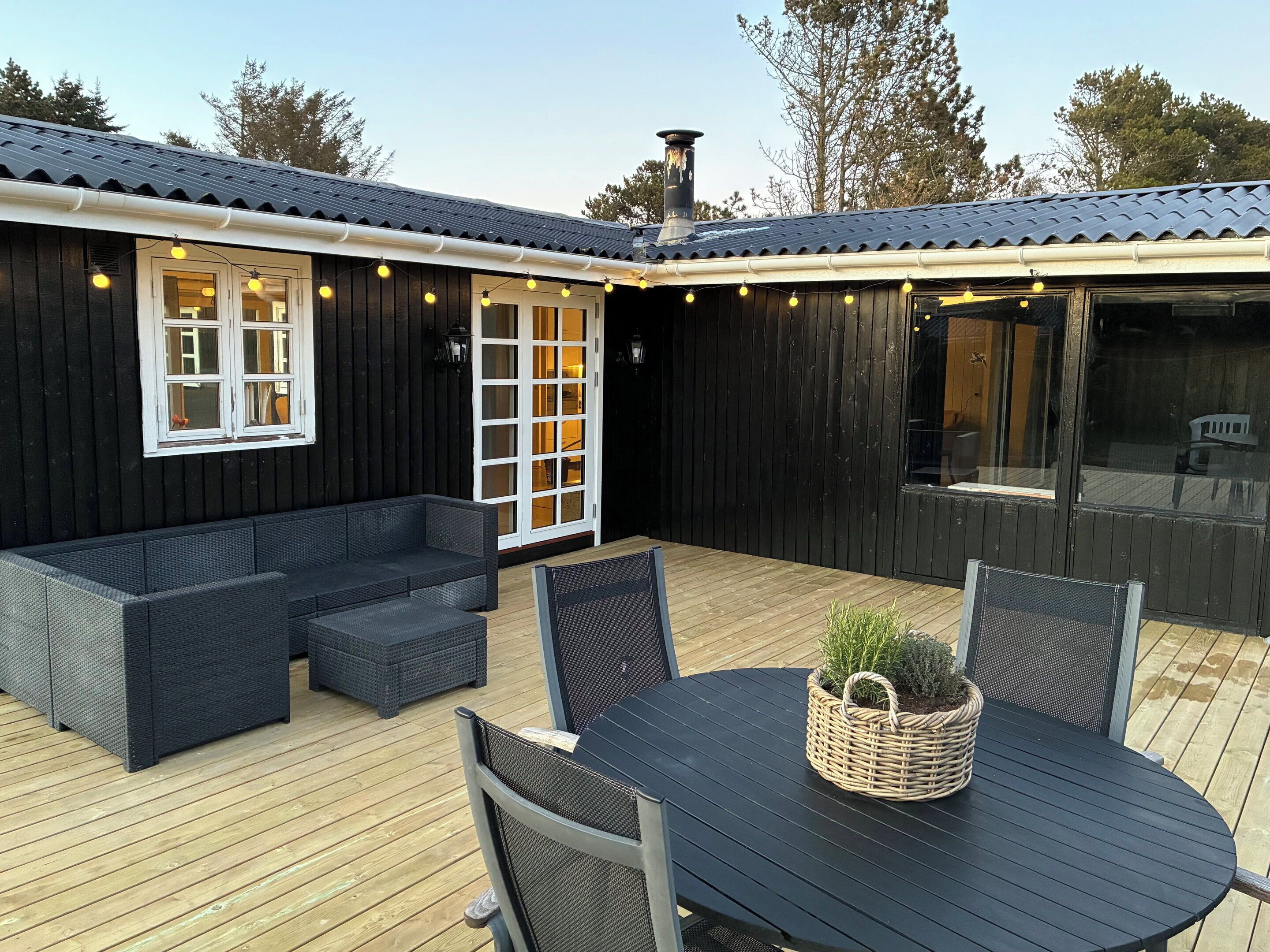 Une terrasse en bois avec des meubles d’extérieur, une table agrémentée d’une plante et un bâtiment doté d’une cheminée.