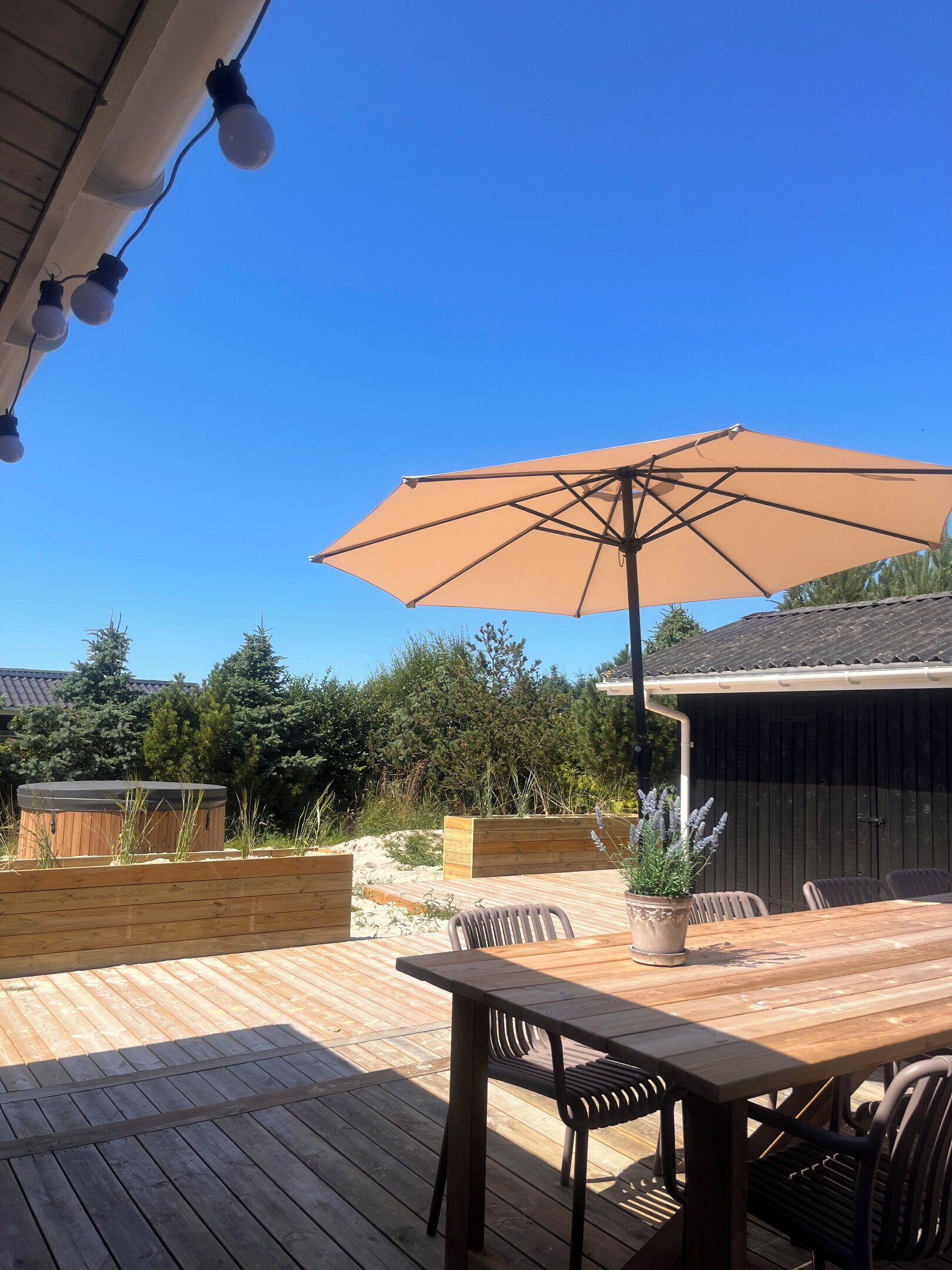 Un patio al aire libre con mesa y sillas de madera, un paraguas grande y un jacuzzi.