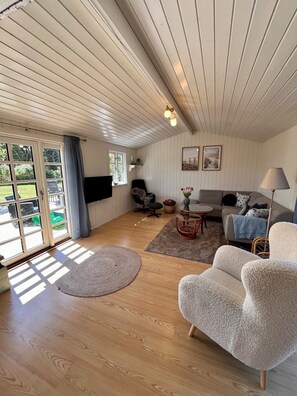 A spacious living room with a wooden floor, a sofa, a chair, a coffee table, and a television. - Renovated holiday home in Grønhøj with a hot tub. (Løkken)