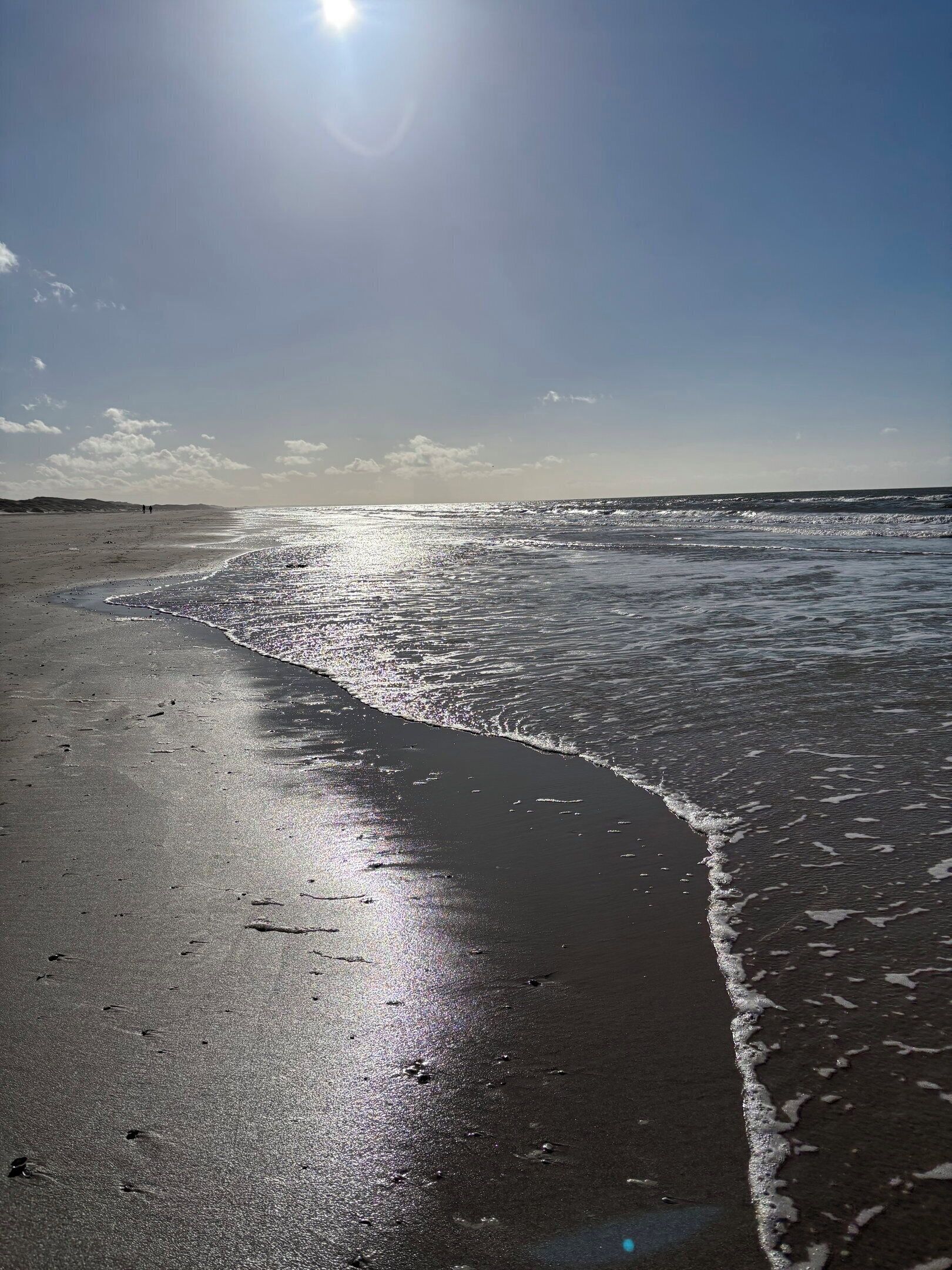 A beach with a clear sky and sunlight reflecting on the water.