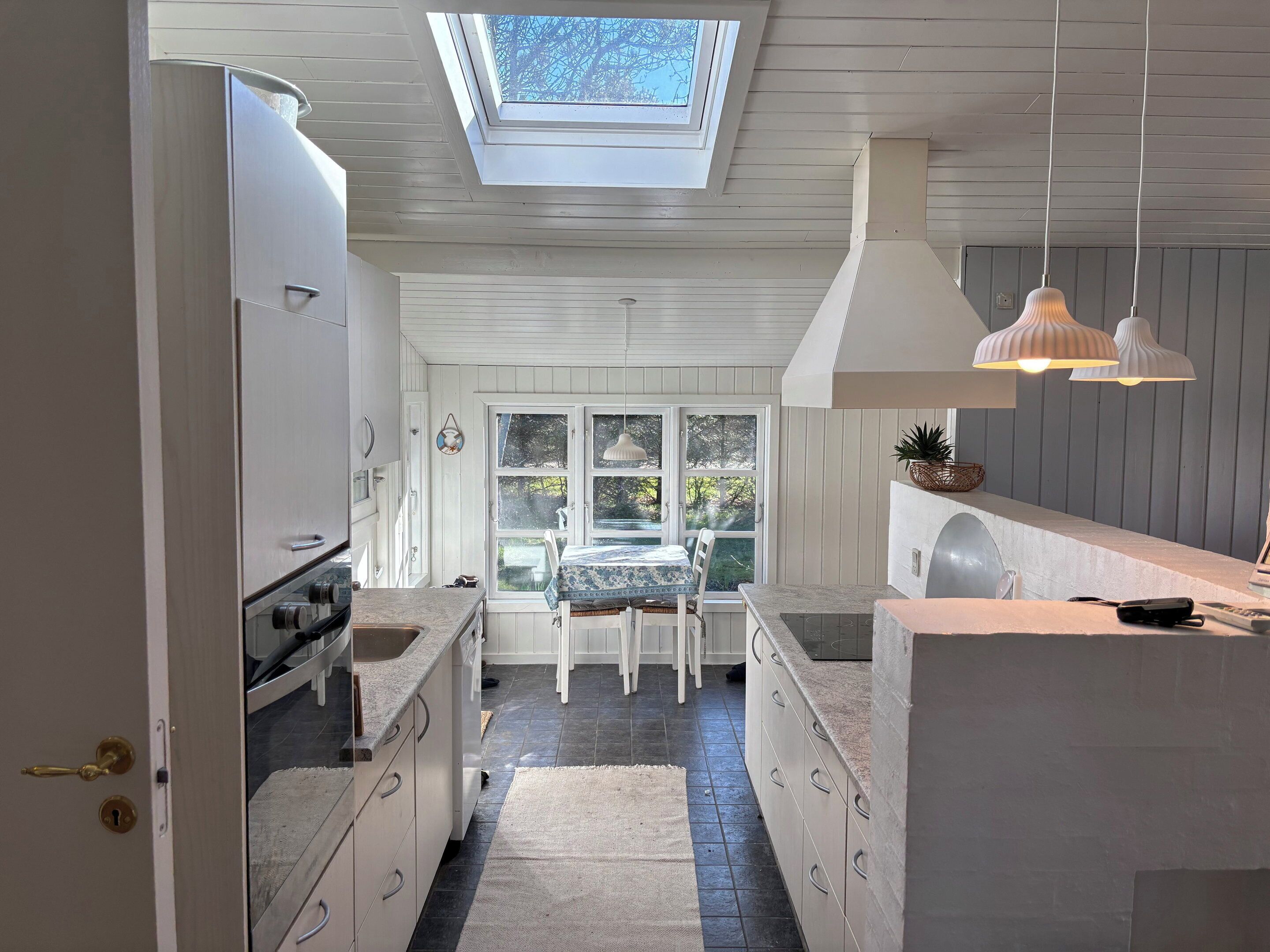 Een keuken met dakraam, witte kasten, een eettafel en hanglampen.