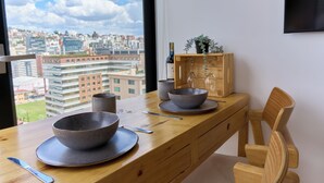 Una mesa de comedor con cuencos y una botella de vino, una silla de madera y vistas a un paisaje urbano a través de una ventana.