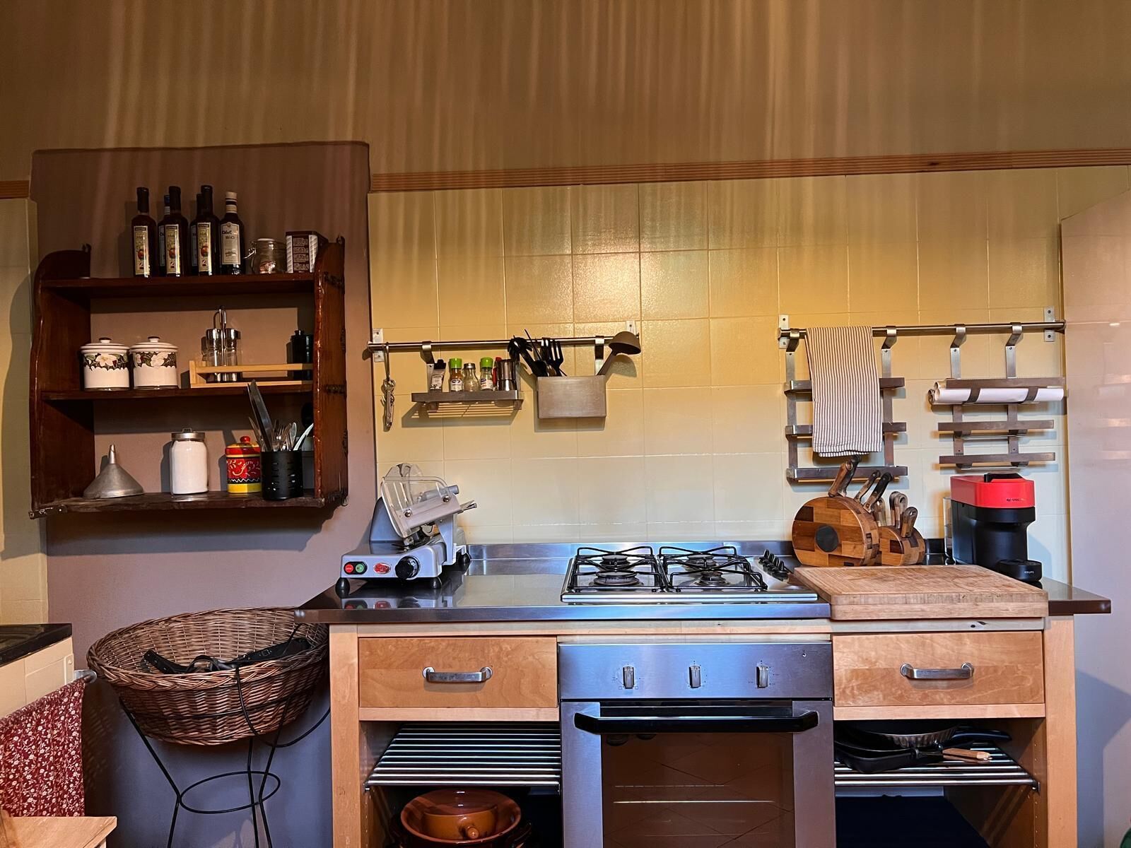 Une cuisine équipée d’une cuisinière à gaz, d’un four et de divers ustensiles. On y trouve des étagères avec des bocaux et un panier.
