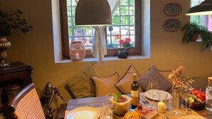 A dining area with a table set for two, a window with a view of the outside, and a hanging lamp above the table.