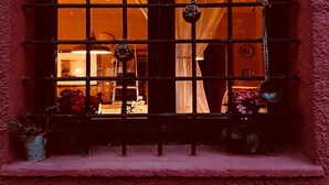 A window with metal bars and a view of a room with a bed and a nightstand.