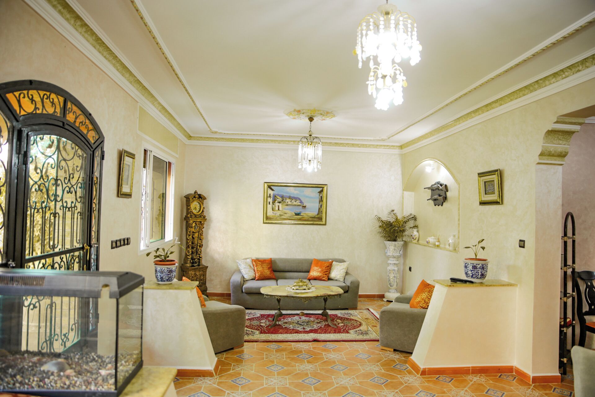 Un salon comprenant un canapé, deux fauteuils, un lustre, une horloge et un tableau accroché au mur.