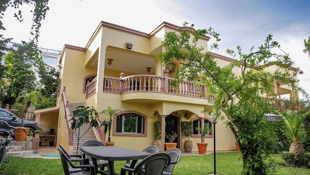 Ein zweistöckiges Haus mit Balkon, Sitzgelegenheit im Freien und Blumentöpfen.