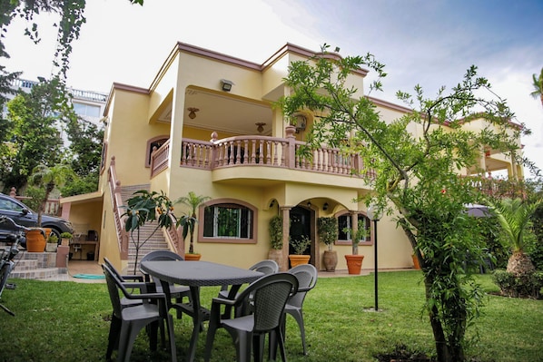 A two-story house with a balcony, outdoor seating, and potted plants.