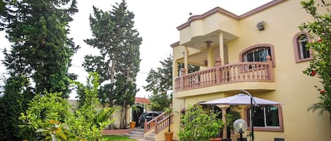 Un edificio de dos pisos con balcón, escalera y un patio con mobiliario exterior.