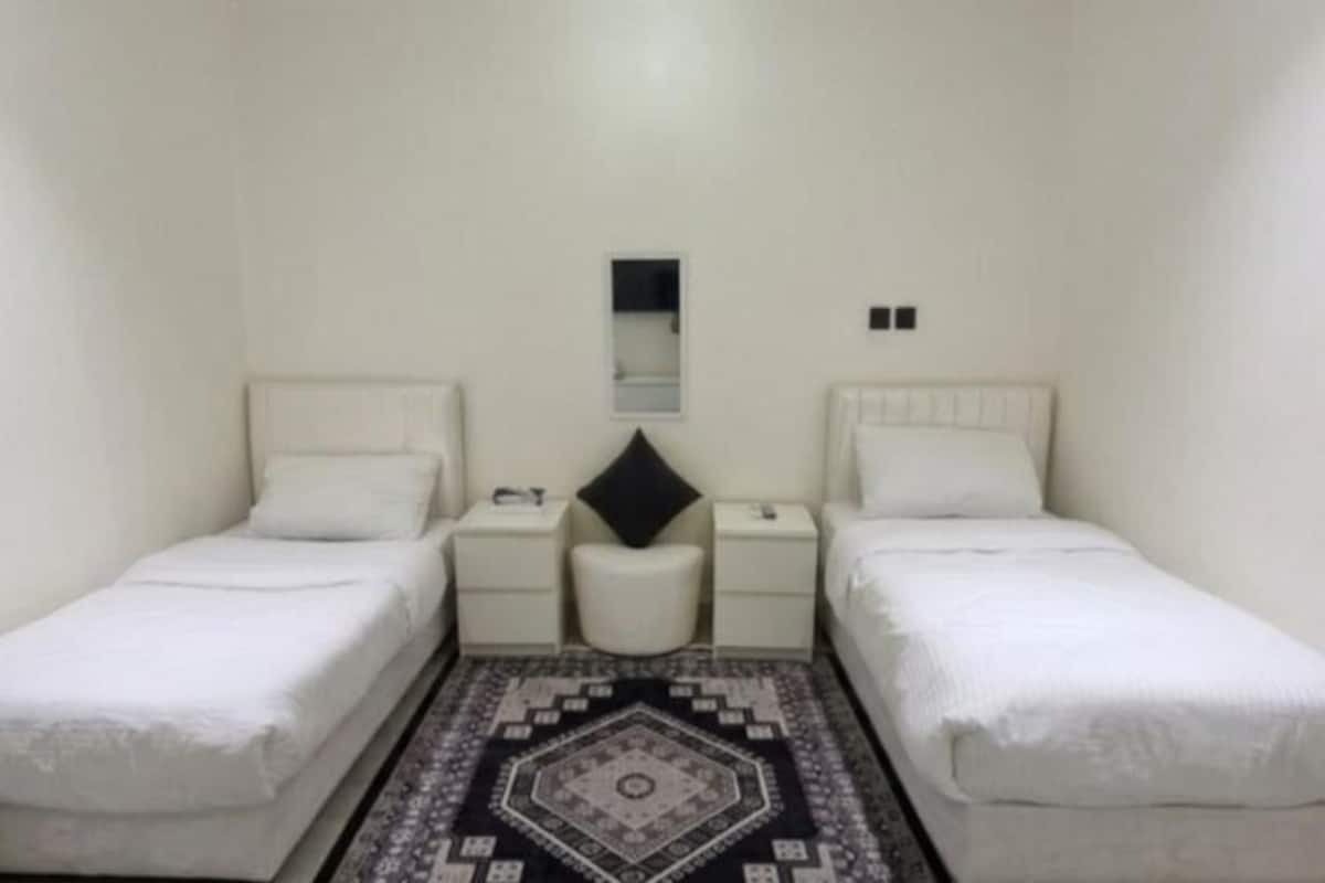 A twin room with two beds, a small table, a chair, a mirror, and a patterned rug.