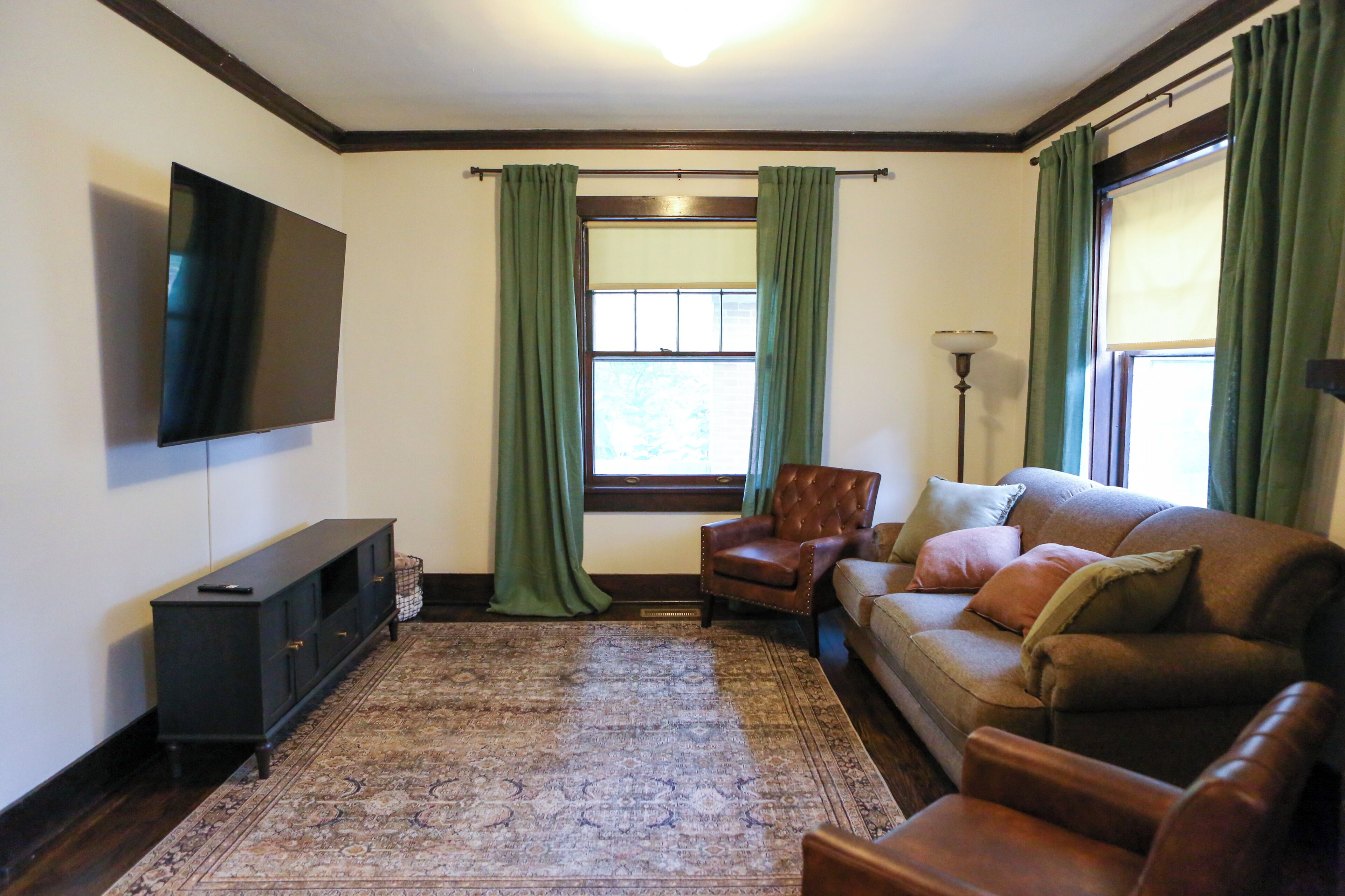 A living room with a television mounted on the wall, a sofa, a chair, and a patterned rug.