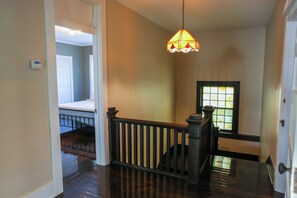 A hallway with a wooden railing, a hanging light fixture, and a door leading to another room.