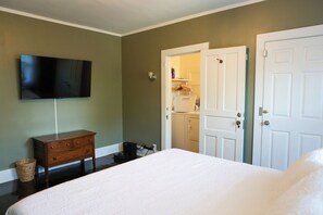 A bedroom with a bed, a dresser, a television mounted on the wall, and a door leading to a bathroom.