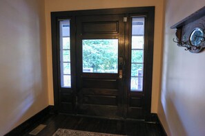 A black wooden door with a glass panel and a small window, leading to a hallway with a wooden floor and a wall-mounted clock.