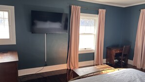 Een hotelkamer met een bed, een bureau, een stoel, een wandtelevisie en een raam met gordijnen.