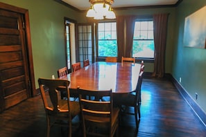 A conference room with a large wooden table and chairs, a chandelier, and windows with curtains.