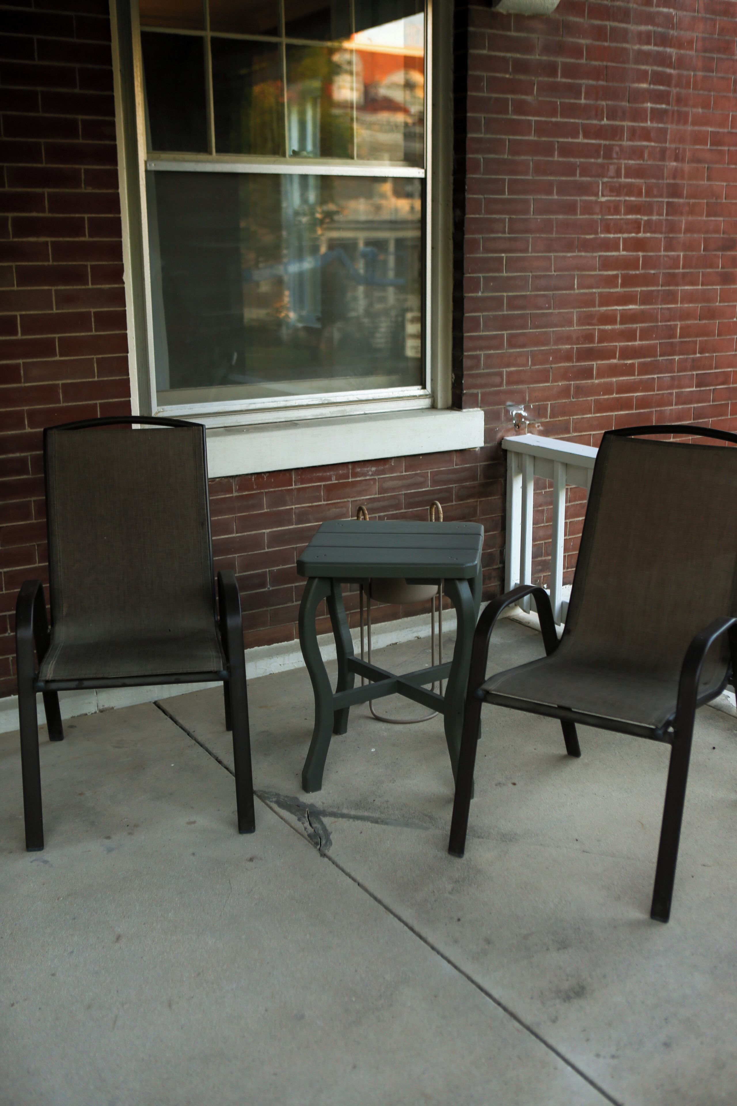Two chairs and a small table outside a building with a brick wall and a window.