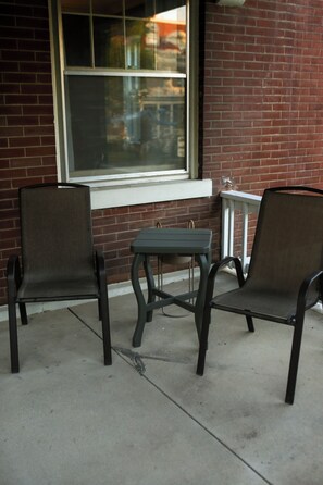 Two chairs and a small table outside a building with a brick wall and a window.