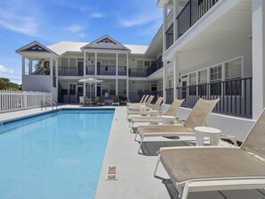 A pool with lounge chairs and umbrellas, a white fence, and a building with balconies. - Poinciana Place #222 | Near Beach, Great Location, Resort Amenities (Miramar Beach)