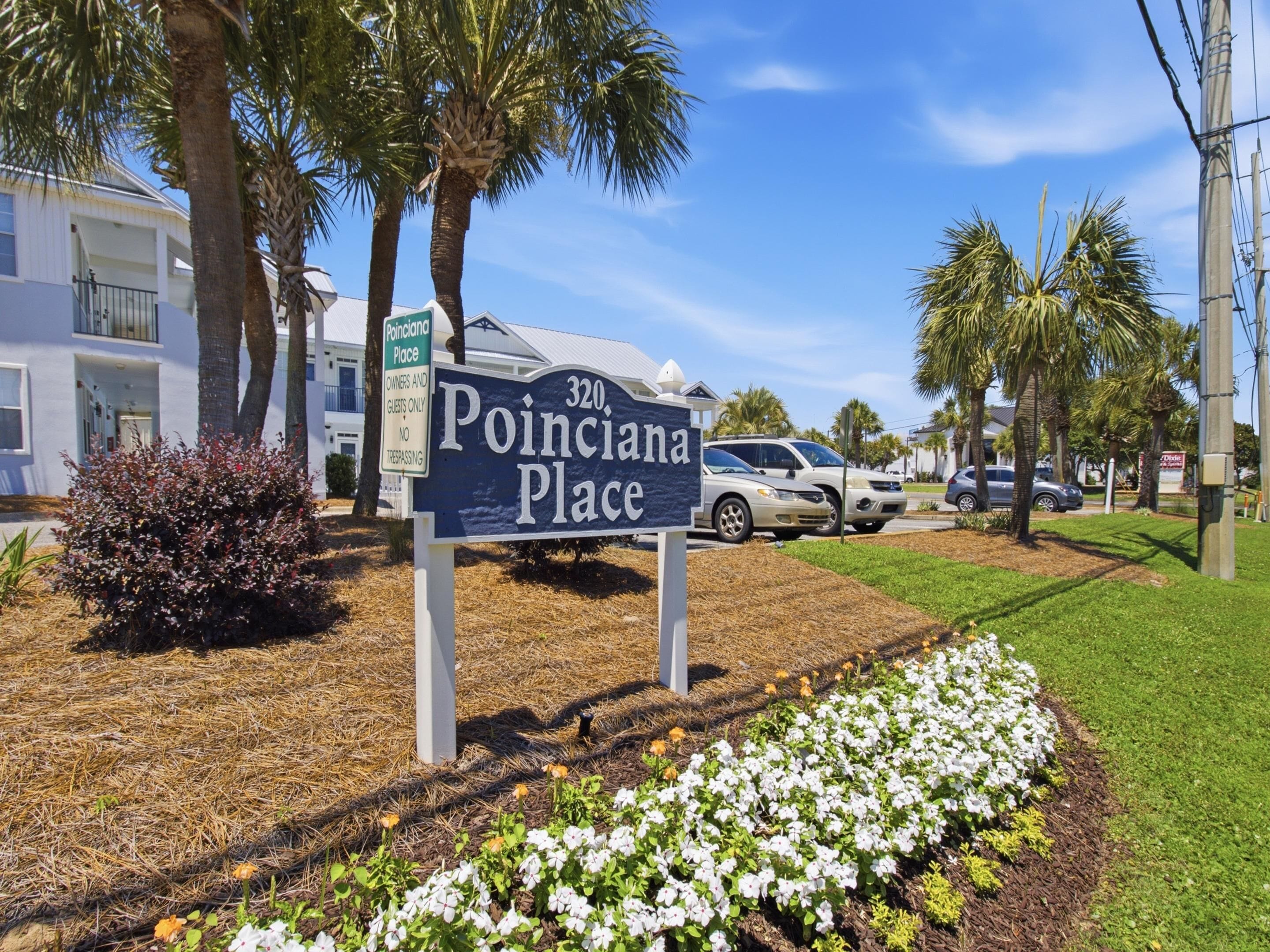 A sign for 'Poinciana Place' with a clear view of the surrounding area including a building, parked cars, and a landscaped garden.