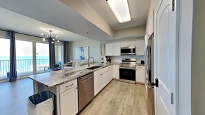 Une cuisine moderne dotée d’un grand îlot central, d’appareils électroménagers en acier inoxydable et offrant une vue sur l’extérieur.