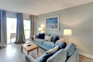 Ein Wohnzimmer mit einer Couch, zwei Lampen, einem Gemälde und Blick durch ein Fenster.