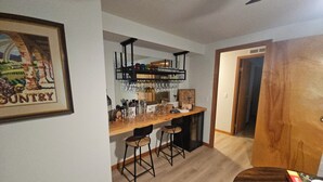 Uma cozinha com bancada de madeira, banquetas de bar e uma estante suspensa para vinhos.