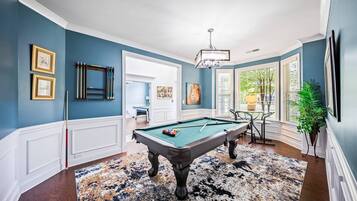 Une table de billard dans une pièce aux murs bleus, avec un tapis à motifs et un lustre.