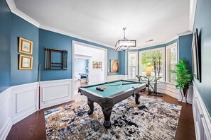 A pool table in a room with blue walls, a patterned rug, and a chandelier. - Luxury Concord Retreat | Spacious Home with Hot Tub, Game Room, Pool Table, Fire Pit, Grill & More! (Concord)