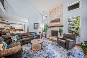 A spacious living area with a stone fireplace, a dining area, and a kitchen with white cabinets. - Luxury Concord Retreat | Spacious Home with Hot Tub, Game Room, Pool Table, Fire Pit, Grill & More! (Concord)