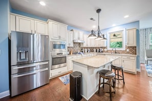 A modern kitchen with stainless steel appliances, a central island with stools, and a view of greenery outside. - Luxury Concord Retreat | Spacious Home with Hot Tub, Game Room, Pool Table, Fire Pit, Grill & More! (Concord)