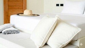 Un lit bien fait, avec du linge de lit blanc, un chapeau de paille et une paire de lunettes de soleil posées sur la tête de lit.