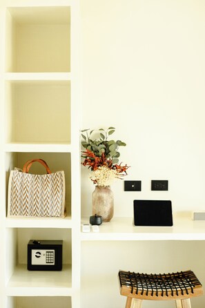 Une étagère avec un sac à motifs, un vase avec des fleurs, une petite boîte noire et un tabouret en bois.