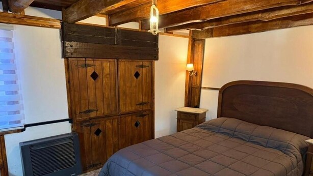 Una camera da letto con un armadio in legno, un letto con copriletto, un termosifone e una lampada a parete.
