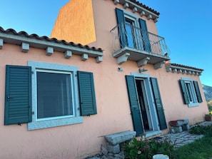 A two-story building with green shutters, a balcony with wrought iron railings, and a stone staircase leading to the entrance. - Villa Cunconi: A unique panorama between the mountains and the sea (Calangianus)