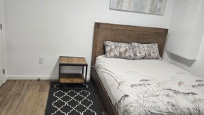 Une chambre à coucher avec une tête de lit en bois, un lit recouvert d’une literie à motifs floraux, une table de chevet et un tapis à motifs géométriques.