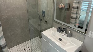 Une salle de bain moderne avec une douche à parois de verre, un grand miroir et un lavabo blanc.