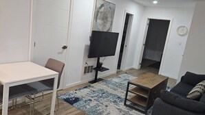 Un salon moderne avec une table blanche, un canapé gris, un téléviseur et un tapis à motifs.