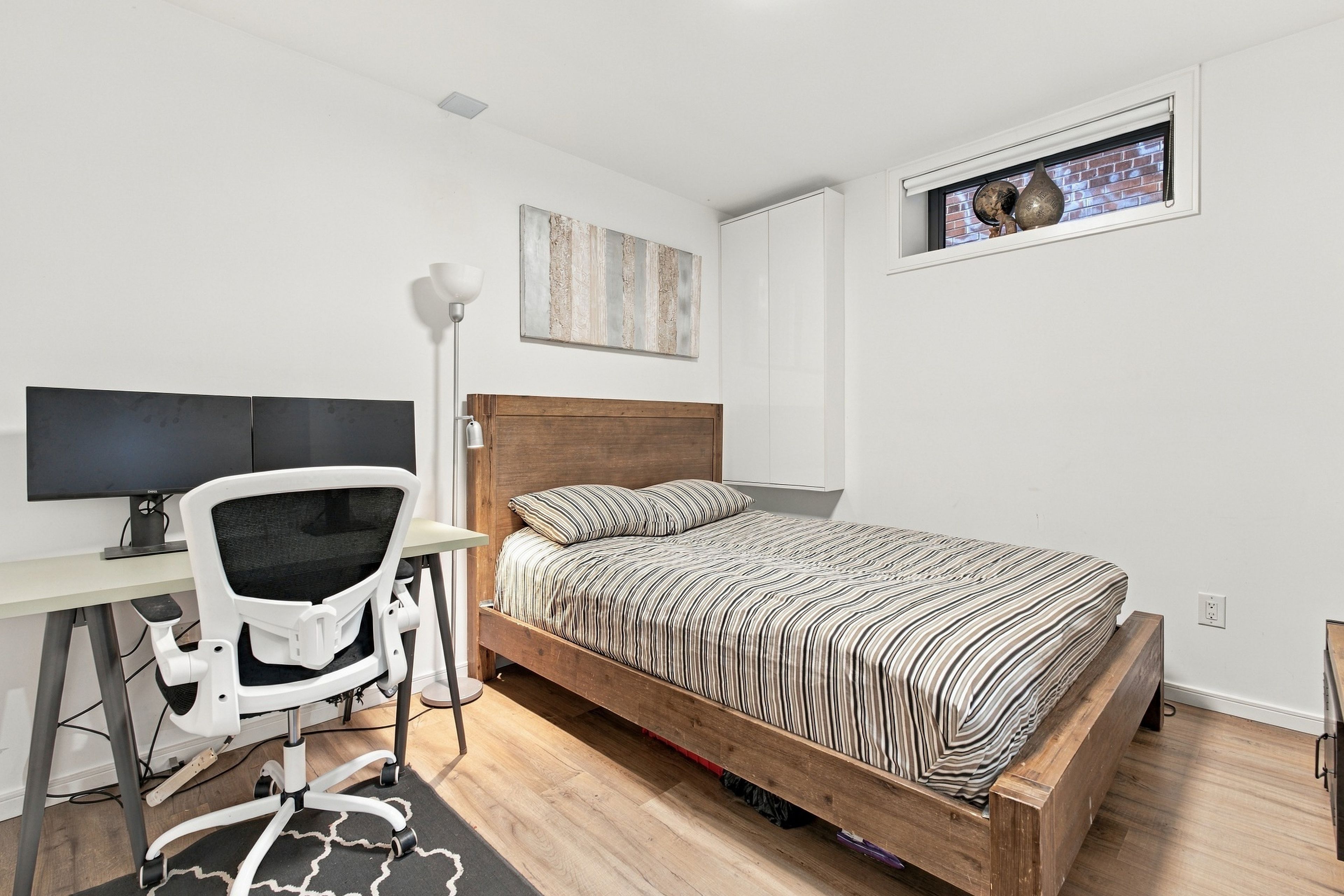 A bedroom with a wooden bed, a desk with a computer, a chair, and a window with a view.
