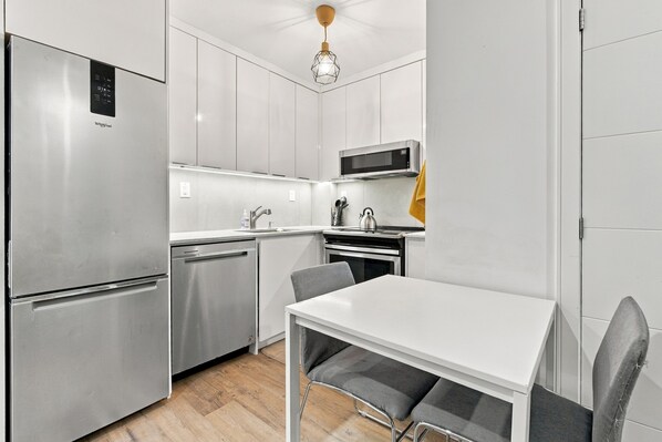 A compact kitchen with a stainless steel refrigerator, a microwave, a sink, and a dining table with chairs.