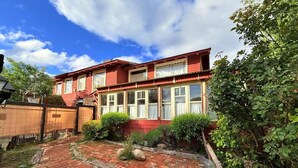 A red two-story house with a brick pathway leading to the entrance, surrounded by greenery. - Casa Tres Coronas: tranquility, independence, warmth, and very spacious rooms. (San Martín de los Andes)