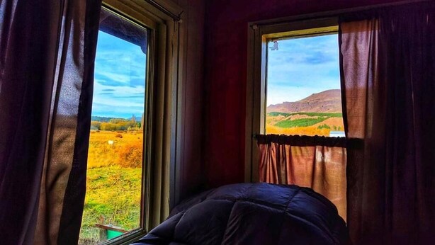 A room with a bed, two windows with curtains, and a view of a landscape. - Casa Tres Coronas: tranquility, independence, warmth, and very spacious rooms. (San Martín de los Andes)
