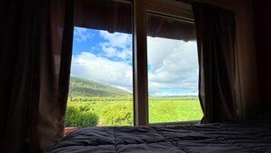 A bed with a view of a green landscape through a window. - Casa Tres Coronas: tranquility, independence, warmth, and very spacious rooms. (San Martín de los Andes)